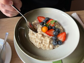 Koseverden & Koselig Cafe, Storgata, Tromsø, Norway - man dipping spoon in tasty breakfast oatmeal served with fresh berries strawberries, blueberries physalis