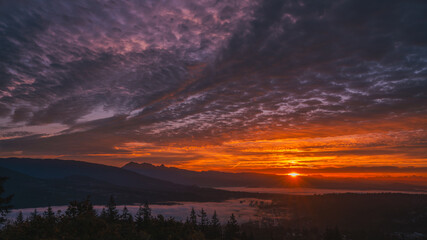 Sunrise over valley shrouded in low-lying cloud with mountains in silhouette on horizon.