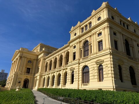 Foto da vista panor&acirc;mica do Museu do Ipiranga em S&atilde;o Paulo, Brasil, com o edif&iacute;cio hist&oacute;rico, jardins e fontes sob um c&eacute;u azul claro. Um s&iacute;mbolo da independ&ecirc;ncia e patrim&ocirc;nio do Brasil.
