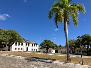 Paisagem histórica em Goiás, Goiás, Brasil, com prédios coloniais antigos e um coqueiro sob um céu azul claro. A foto destaca o rico patrimônio arquitetônico e o charme da cidade. Velha Cadeia.