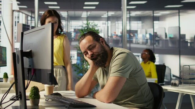 Tired company worker caught falling asleep at desk in office by colleague, laughing about it. Exhausted man sleeping in front of computer screen in workplace, woken up by amused coworker, camera B
