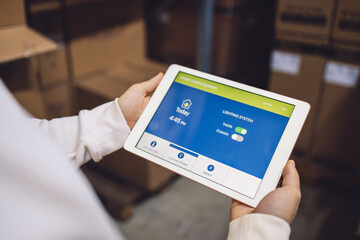 The young female owner and the man in the warehouse check the temperature, energy consumption and lights on a tablet.