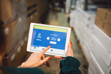 The young female owner and the man in the warehouse check the temperature, energy consumption and lights on a tablet.