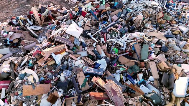 4k aerial view of a large landfill filled with mixed household and construction waste, including furniture, plastic, and other debris. 