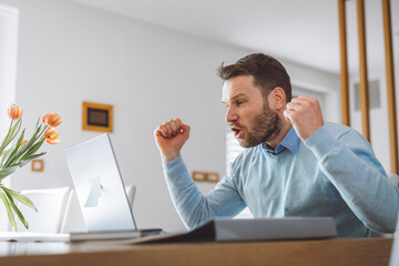 Naklejka premium Excited man full of energy sitting behind laptop with big smile on his face. Overly happy person looking at the laptop. Business success.
