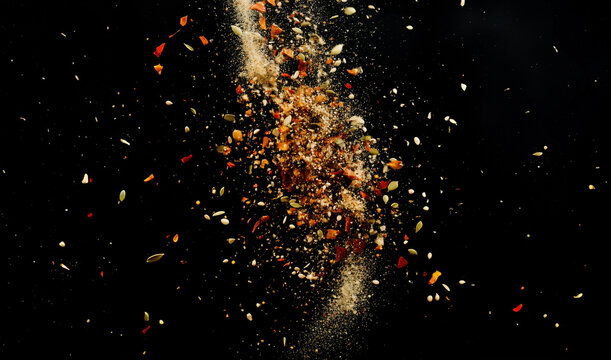 herbs and spices explode into the air isolated on black background - a warm and spicy flavorful blast of seasonings and ingredients for gourmet food