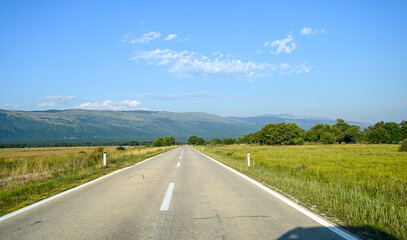 A long straight road in a field. Driving a car in nature. Drivers view on asphalt road in field in summer. 