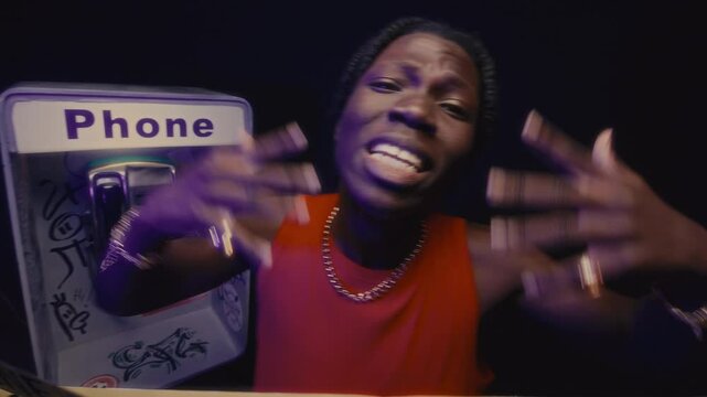 Black rapper performing with intensity behind caution tape at gritty crime scene with street payphone, spitting raw verses with bold gestures directly to camera