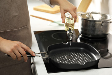 Woman pouring oil into frying pan on cooktop in kitchen, closeup
