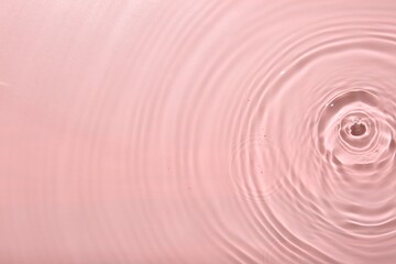 Rippled surface of clear water on pink background, top view