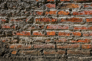 A close-up of an old brick wall partially covered with rough cement, showing a blend of red bricks and gray mortar, creating a rustic and textured architectural background