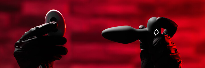 Silicone anal plug with a remote control in a female hand wearing black latex gloves on a black...