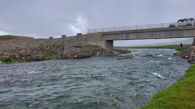 Static shot capturing narrow stream of lake passing under a bridge along the route leading to Deosai Plains, Skardu in Pakistan.