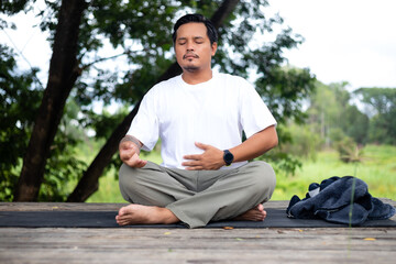 Obraz premium A man is sitting on a mat in a park, with his hands on his stomach