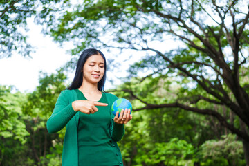 An Asian woman holds a globe in a green forest,symbolizing the importance of preserving...