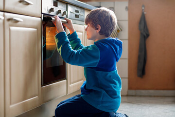 Cute blond boy baking muffins or pie in domestic kitchen. Happy child having fun with helping,...