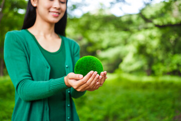 Fototapeta premium An Asian woman holds a globe in a green forest,symbolizing the importance of preserving nature.emphasizes balance between humans, natural resources,sustainable environmental development protect