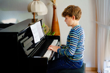 Beautiful little kid boy playing piano in living room. Child having fun with learning to play music...