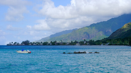 Scenic view of solo boat in turquoise ocean water of lagoon with over water beach huts and mountains on tropical island on Mo'orea, Tahiti in French Polynesia, South Pacific