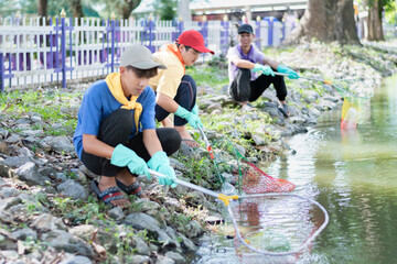 A group of students in volunteer uniforms work together near a pond in their community by using nets to collect plastic bottles and other trash from the water to protect local spaces from pollution.