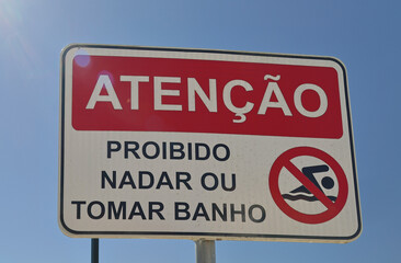 No swimming sign displaying warning in portuguese on blue sky background