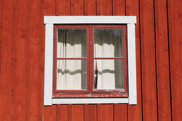 A red  wooden wall with an old window with curtain.