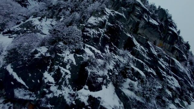 FPV drone glides along a snow-covered cliffside, showcasing rugged terrain at Mont Pinacle