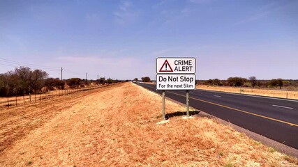 Crime alert warning road sign next to South African highway advising not to stop