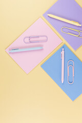 Top view of pink, purple and blue notebooks on yellow background. Pink, yellow and blue pens, paperclips, school, office wallpaper. Flat lay, copy space.