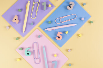 Top view of pink, purple and blue notebooks on yellow background. Colorful pens, paperclips, numbers and pins. School, office wallpaper. Flat lay, copy space.