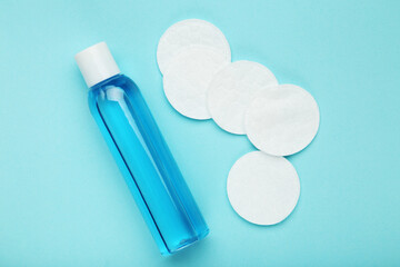 Cotton pads and cosmetic bottle on blue background