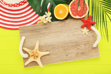 Fresh fruits with starfishes, green leafs, striped hat and wooden tray on green table