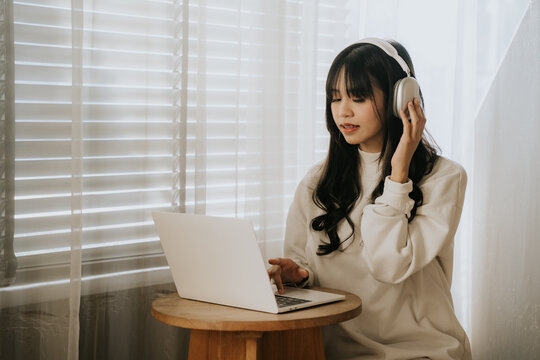 Focused Concentration: A young woman, immersed in her work, sits at her laptop with headphones on, her focused expression and posture conveying deep engagement and productivity.