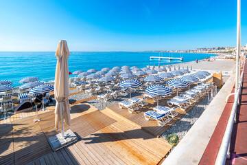 Turquoise sea, blue and white umbrellas, lounge chairs, and the pebble beach along the paved Promenade des Anglais and Bay of Angels, at the Cote d'Azur French Riviera, in Nice, France.  © Kirk Fisher