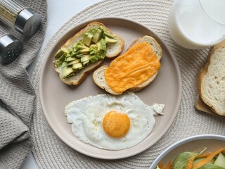 Healthy breakfast with fried egg, vegetables and bread on white wooden table.