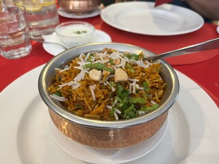 Rice biryani in a copper bowl on a restaurant table