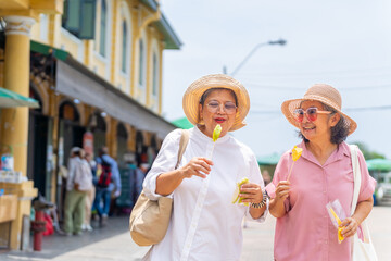 Group of Happy Asian senior woman tourist enjoy outdoor lifestyle travel in the city on summer holiday vacation. Elderly retired women travel shopping at street market and eating street food together.