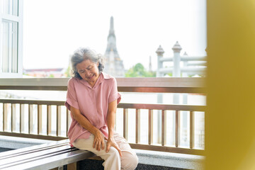 Travel and health insurance concept. Asian senior woman tourist travel Buddha temple in Thailand on summer holiday vacation. Elderly woman get injury knee pain or leg cramp during travel in the city.