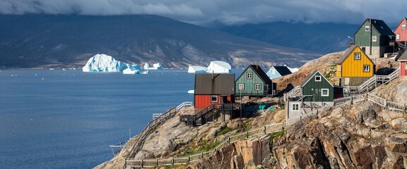 Baffin Bay, the colorful typical houses in the small village of Uummannaq, the Greenland. Icefjord in Greenland and the silhouette of the high mountain ridge in the background under the blue melting g
