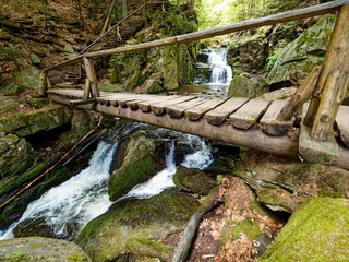 The Resov waterfalls cascade down a rocky cliff in Czech Moravia. A wooden footbridge provides a scenic view of the falls.