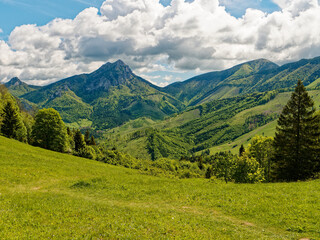 View of the Rozsutec mountain in the Mala Fatra mountains in Slovakia. The landscape shows lush green hills, dense forests, and vibrant fields under a sky filled with fluffy clouds on a sunny day.

