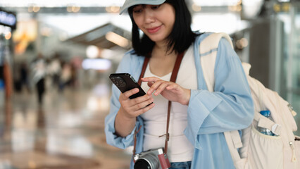 Smiling young woman using mobile phone, waiting for boarding in airport terminal. Travel and vacation concept.