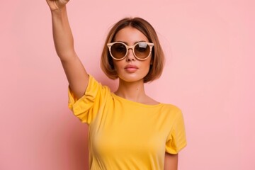 Fototapeta premium A young woman embodies determination as she raises her fist in a powerful protest stance, wearing oversized sunglasses against a soft pastel backdrop, advocating for social change.