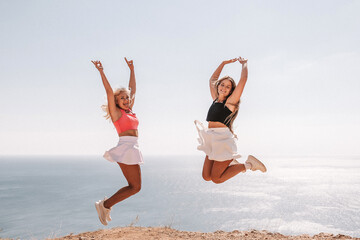 Obraz premium Two women are jumping in the air on a beach. The sky is blue and the ocean is in the background. Scene is joyful and energetic.