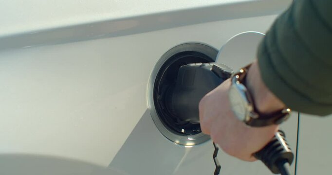 Man plugging in electric car at home at electro charging station. Luxury white electrical car recharging. Environmentally conscious man charging his electric vehicle.