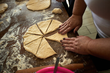 A group of people stand around a wooden table and make buns from dough and jam.