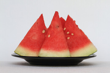 Some slices of watermelon (Citrullus lanatus) on black plate.