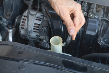 Man checking the windshield washer fluid of a car.