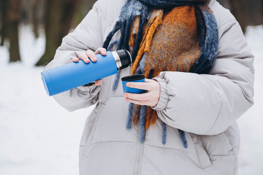 Young woman pouring a drink from a thermos in winter