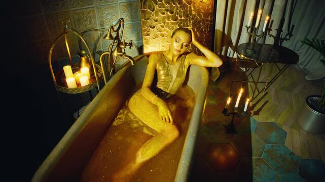 Glamour Beauty fantasy woman face, body covered in gold paint. Golden shiny skin. Sexy fashion model wet girl goddess lies bathed in liquid gold bathroom water. royal lady metallic luxury makeup 4k